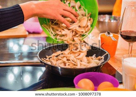 Female hand puts sliced mushrooms on frying pan