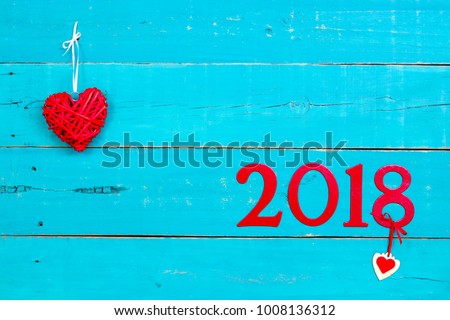 Year 2018 in bold red by red hearts hanging by ribbon on antique rustic teal blue wood background; message board or sign with Valentines Day holiday and love concept and painted copy space