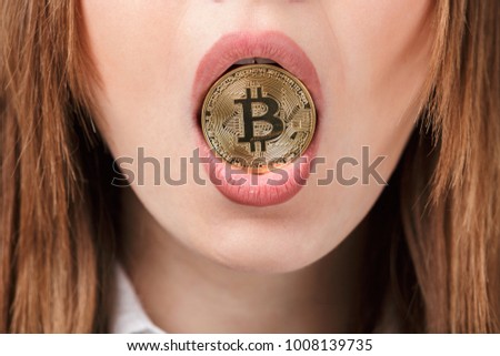 Close up of a woman holding golden bitcoin in her mouth isolated over gray background