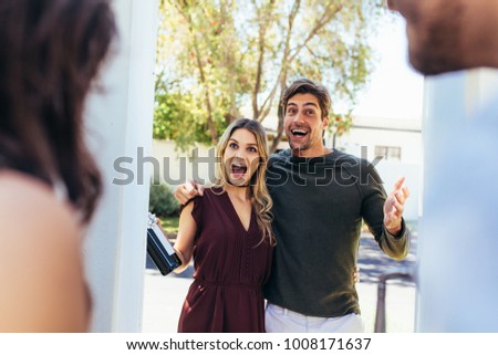 Excited couple at entrance door with bottle of wine. Friends being welcomed by couple at the door. Attending friend's housewarming party. Royalty-Free Stock Photo #1008171637