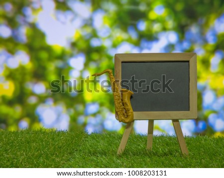 Blackboard is decorated with saxophone on a wooden stand in the lawn. /Play music in the garden 