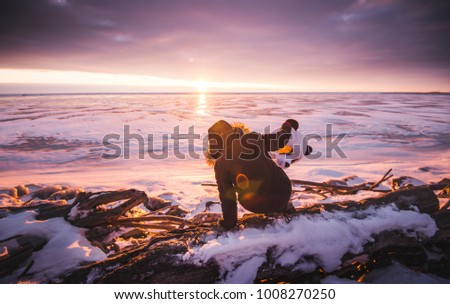 Young beautiful girl in a black jacket and  panda big head wanders the snowy frozen cover places with the sunset over the distance.