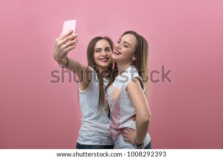 Twins do selfie on phone on a pink background