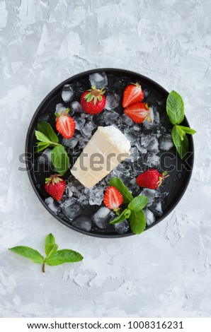 Ice cream with strawberries, mint and ice on dark metal tray. Overhead shot
