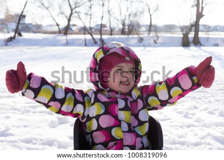 Happy little girl on sled on winter and snowy background. Child sledding