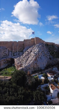 Aerial spring photo of iconic ancient rock of Acropolis hill and the Parthenon, with beautiful scattered clouds and Greek flag waving, Athens historic center, Attica, Greece