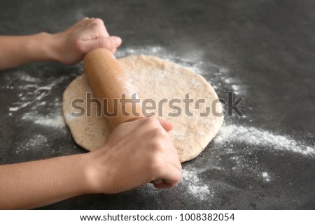 Woman rolling dough with poppy seeds on table, closeup