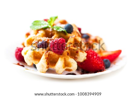 Belgian waffles with syrup, strawberries, raspberries, mint and icing isolated on white background close up.
