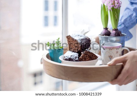 Chocolate cupcake with sugar and coffee. Breakfast on a wooden tray and flowers. View from the window to the city. Free space for text or a postcard.