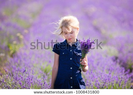 Blonde girl in the blue dress in the field of lavander with a small bouqet of flower