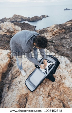 Professional stock aerial photographer, urban adventurer and location explorer, traveler unpacks backpack with expensive equipment and drone, ready to fly over oceanside and inspiring scenery