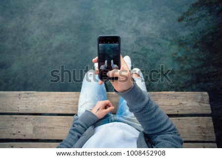 POV shot of man making photo of his sneakers hanging over water on smartphone , to share on social media or internet website, mobile photography for amateurs