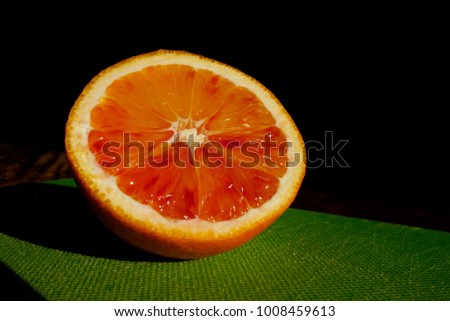 top view of an half orange fruit on a green chopping board, illuminated by the sun light.