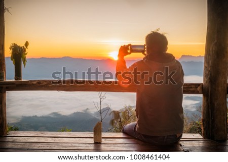 silhouette of man hands holding mobile phone at sunset above winter mountains. male makes a photo on your phone. The glare of the sun illuminate the silhouette.

