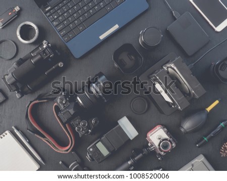 top view of work space photographer with mirrorless camera system, flash, battery charger, external harddisk,  camera cleaning kit, memory card, and camera accessory on black table background.
