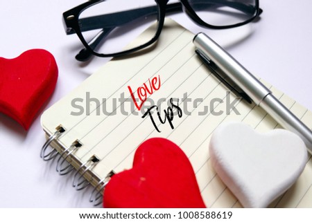 Top view of red and white wooden handcraft heart symbol,pen and sunglass on open book written with 'LOVE TIPS' on white background. Valentine's day theme.