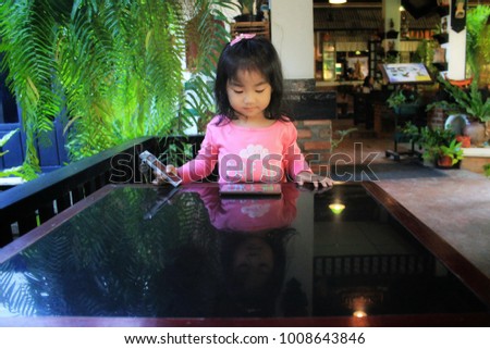  The little girl  watching the cell phone on a black glass table,Girl holding a room key