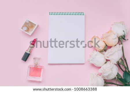 Notebook, perfume, cosmetics and roses on a pastel pink background. Beauty blog