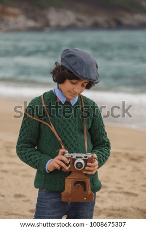 Teenager wearing flat cap and green sweater, holding vintage film camera in his hands. Vertical composition.