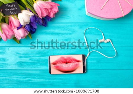 Valentine's Day background with bouquet of tulips and a gift box.Message with a kiss.Mobile phone and headphones in the shape of heart.