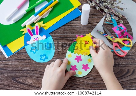 A child is holding an Easter egg gift with a chicken and Easter bunny toy. Handmade. Project of children's creativity, handicrafts, crafts for kids. Royalty-Free Stock Photo #1008742114