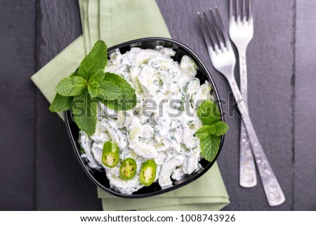 Traditional Indian cuisine. Homemade cucumber raita with yoghurt, garlic, mint, cilantro and spices on black slate background. Greek tzatziki sauce. Copyspace, top view.