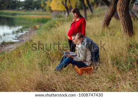 Cheerful family with little boy smiling happily looking at laptop screen walking in park and sat down on a red old leather suitcase