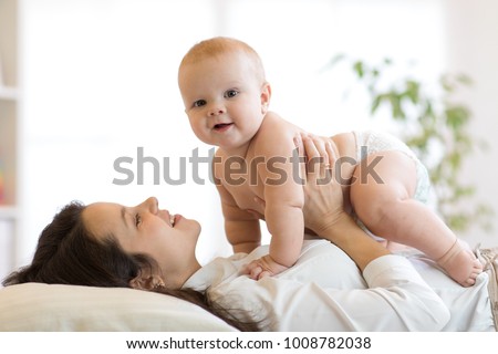 Mom and baby boy playing in sunny bedroom. Parent and little child kid relaxing at home. Family having fun together.