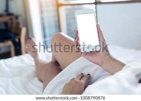 Mockup image of woman's hands holding cell phone with blank desktop white screen while lying in a white bed with feeling relaxed