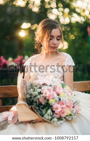 Young girl in wedding dress in park posing for photographer. Sunny weather, summer