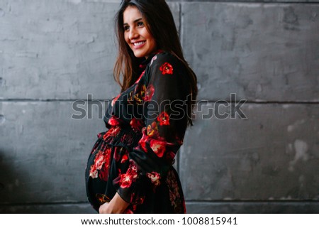 Stylish pregnant woman in a beautiful dress standing on gray background