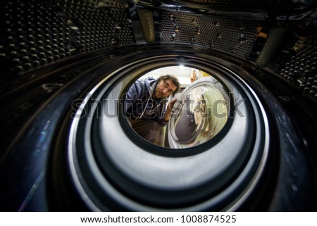 The man looks into the empty washing machine. View from the inside of washing machine. Inside the modern equipment concept. Opening the door of washing machine. Creative show of washing machine.