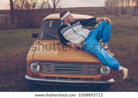 guy in the nineties lies on the hood of an old car Royalty-Free Stock Photo #1008893713