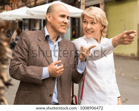 glad senior couple taking promenade and point their fingers outdoors