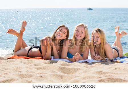 Three young smiling girls in swimwear lying together on a beach. Focus on all persons 