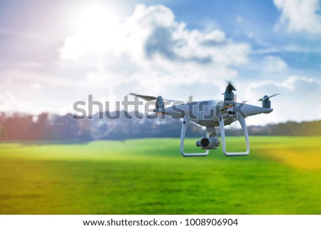 Photo of a flying white professional quadcopter drone camera in front of green grass and forest