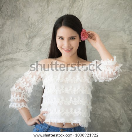 Beautiful asian young girl with a pink english rose  flower on her ear smiling on bare mortar background