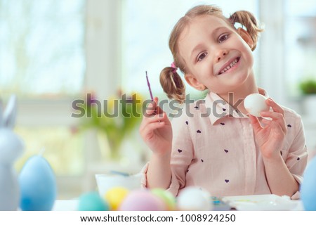 Happy pretty child girl having fun during painting eggs for easter in spring at home