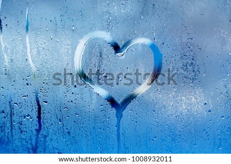 Hand draw a heart and drops of water on the glass. Condensation and raindrops on the window, shallow depth of field