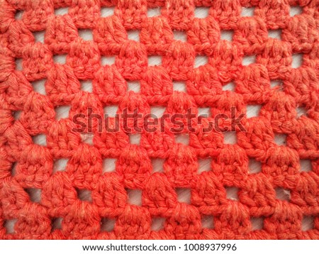 Texture or background of an orange crocheted rug in contrast to white floor.