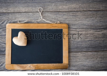 Wooden heart lying on black chalkboard with wooden frame. 