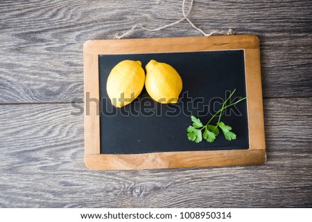 Two lemons next to each other with a coriander leave on a black chalkboard with a wooden frame. Wooden textured background.