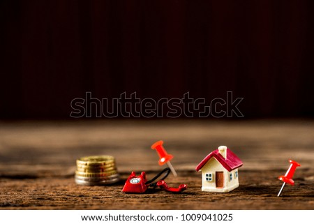 selective focus of miniature tiny home and blurred of stack coins with vintage telephone with red pin on wooden floor,  Image for real-estate management  concept.