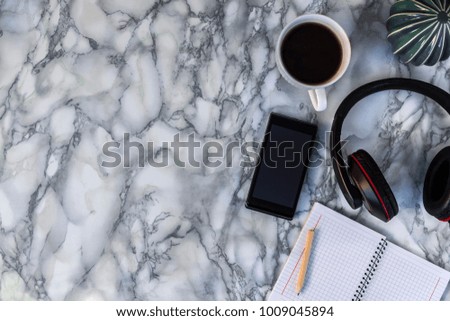 marble desk with ceramic cactus, white circular notebook, lead, coffee cup, headphones from above