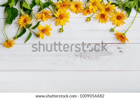Yellow daisy flowers on light wooden background. High top view.