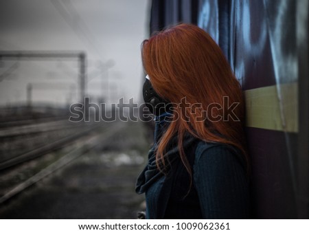 A red haired girl wearing an anti-pollution mask in a very polluted rail yard area. Royalty-Free Stock Photo #1009062361