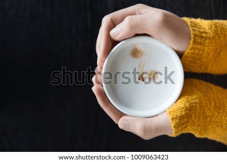 Close up Woman holding cup of hot coffee on dark wooden table, closeup photo of hands in warm sweater with mug, winter morning concept, top view