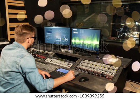 music, technology, people and equipment concept - man at mixing console in sound recording studio over lights