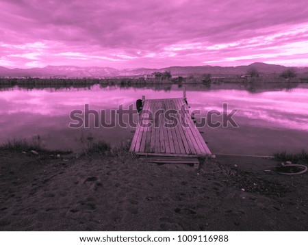 Pink sunset and old fishing wooden pier and river on a background of mountains. Meditative relaxing natural landscape