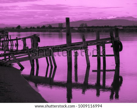 Purple sunset and old fishing wooden pier and river on a background of mountains. Meditative relaxing natural landscape